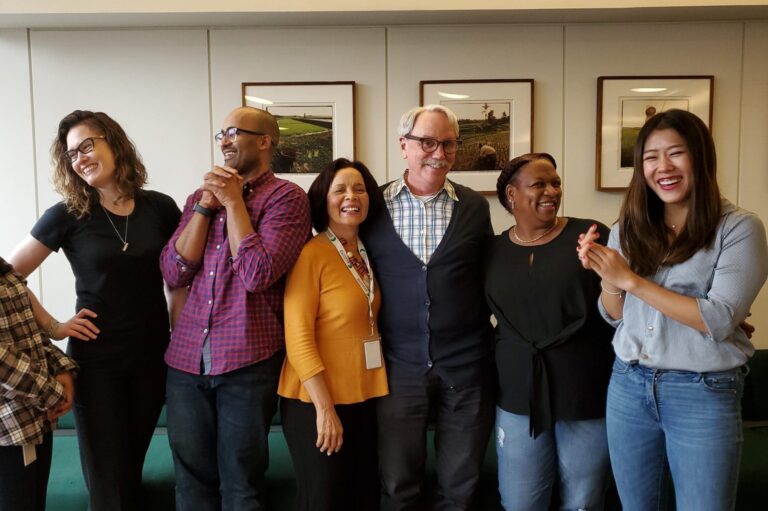 A group of men and women with their arms around each other laughing together.