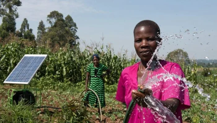 two women in a field and one is holding a water hose spraying water.