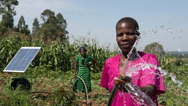 two women in a field and one is holding a water hose spraying water.