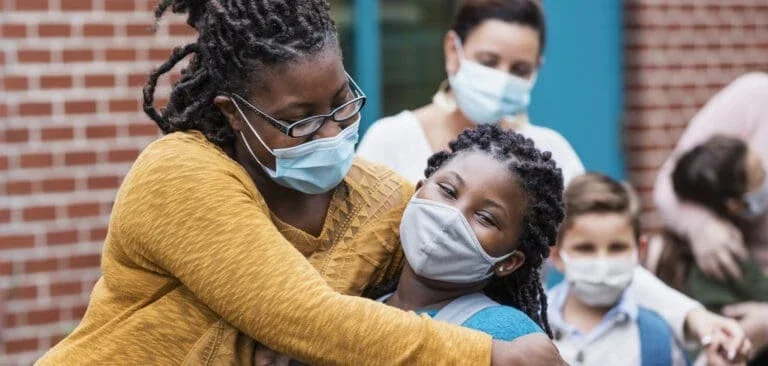 woman with face mask hugging a child with a mask on the side