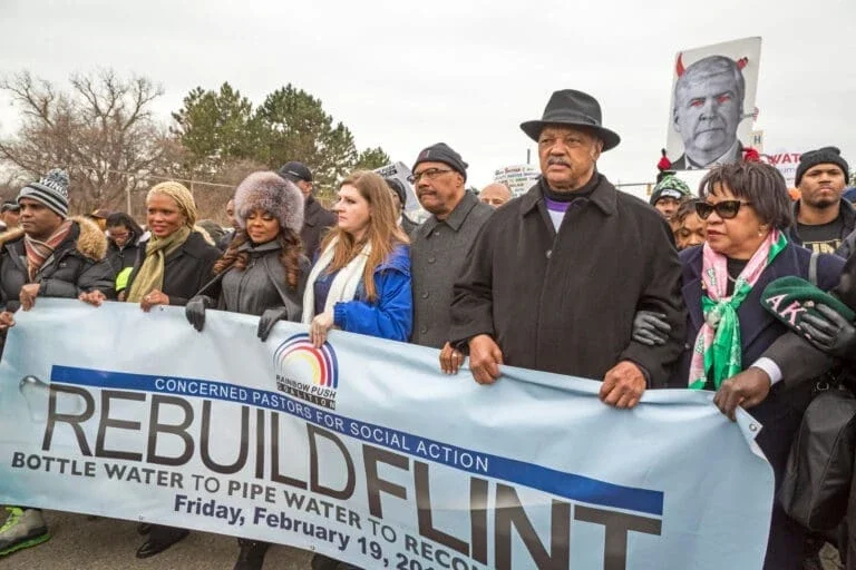 Image is of a group of men and women holding up a sign that says 