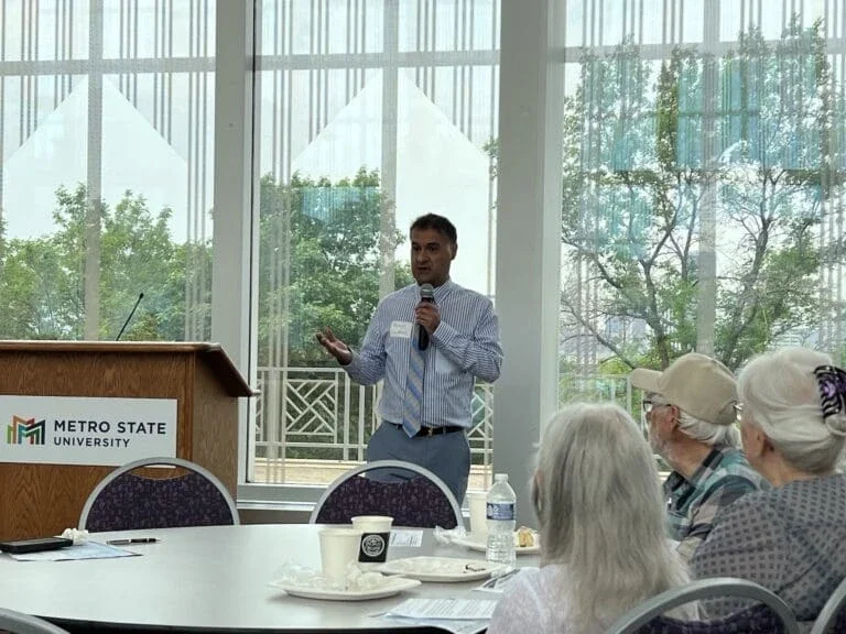 man standing at a podium with microphone in hand speaking to a group of people