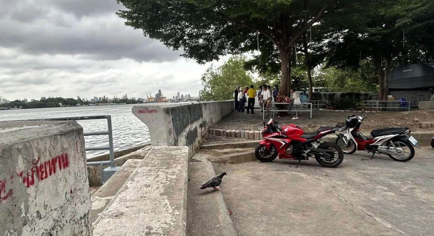 two moto vehicles parked next to a body of water with a group of people sitting at a table in the background