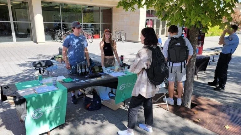 young man and woman standing at a booth on a campus talking to a young man and woman