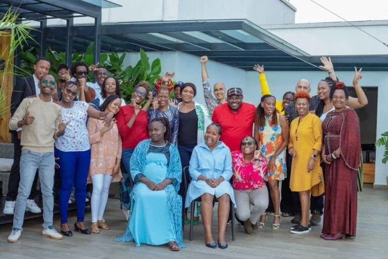 group of people posing for a photo on a rooftop terrace; some are standing while others are seated, and they are all smiling and raising their hands in celebration