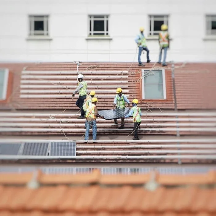 workers in safety gear install solar panels on a rooftop with a white building facade in the background